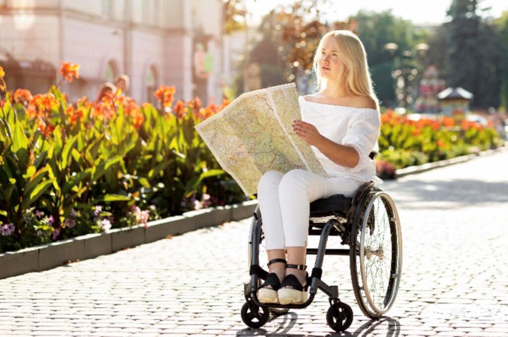Stylishly dressed woman reading a tourist map while sitting in a wheelchair on cobble stoned street.